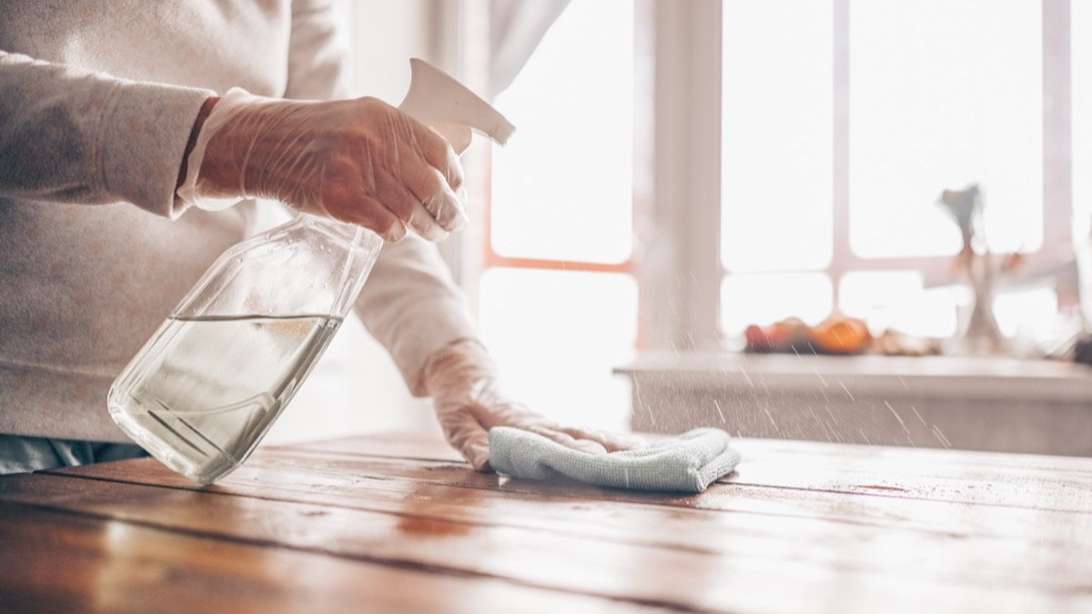 Spraying sanitiser onto a surface and wiping with a cloth