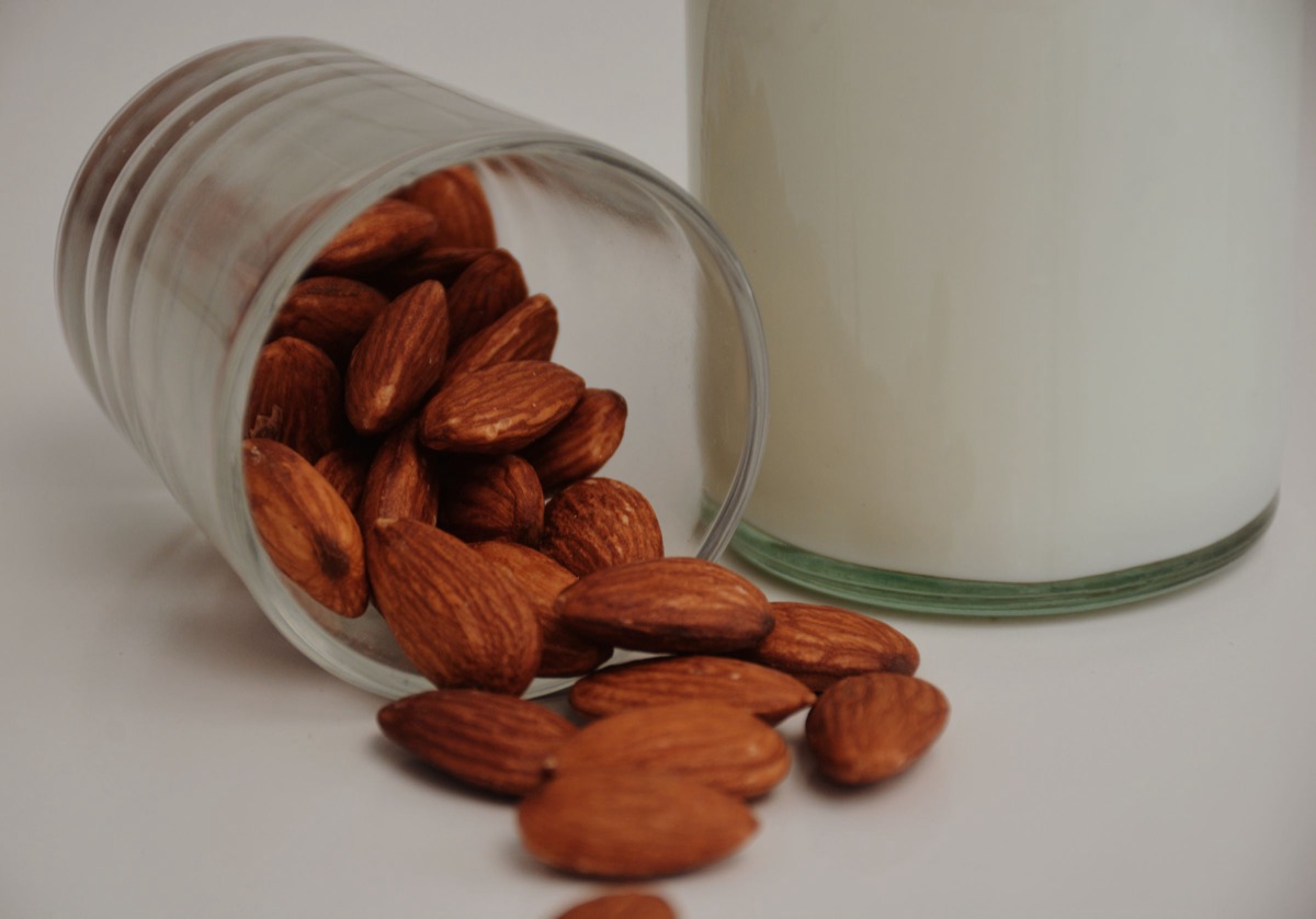 A glass tipped over with almonds spilling out beside a bottle of milk