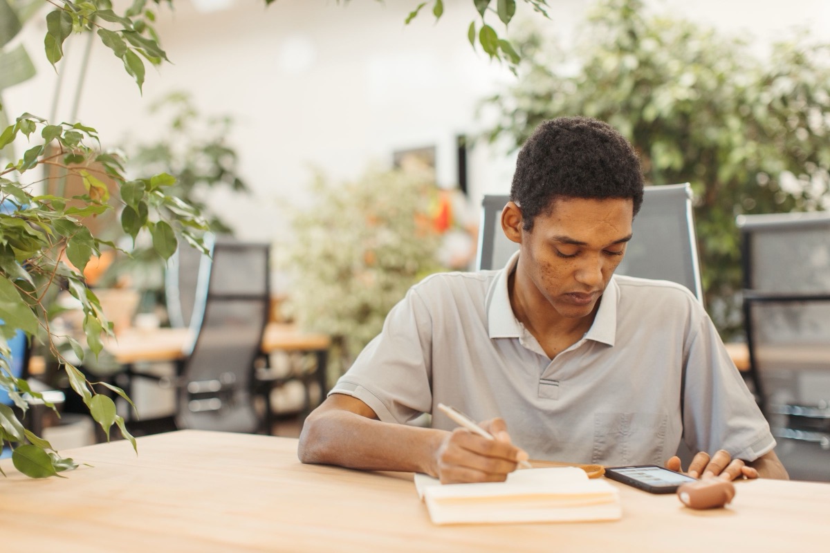 A young man studying at a table with a notebook and his phone