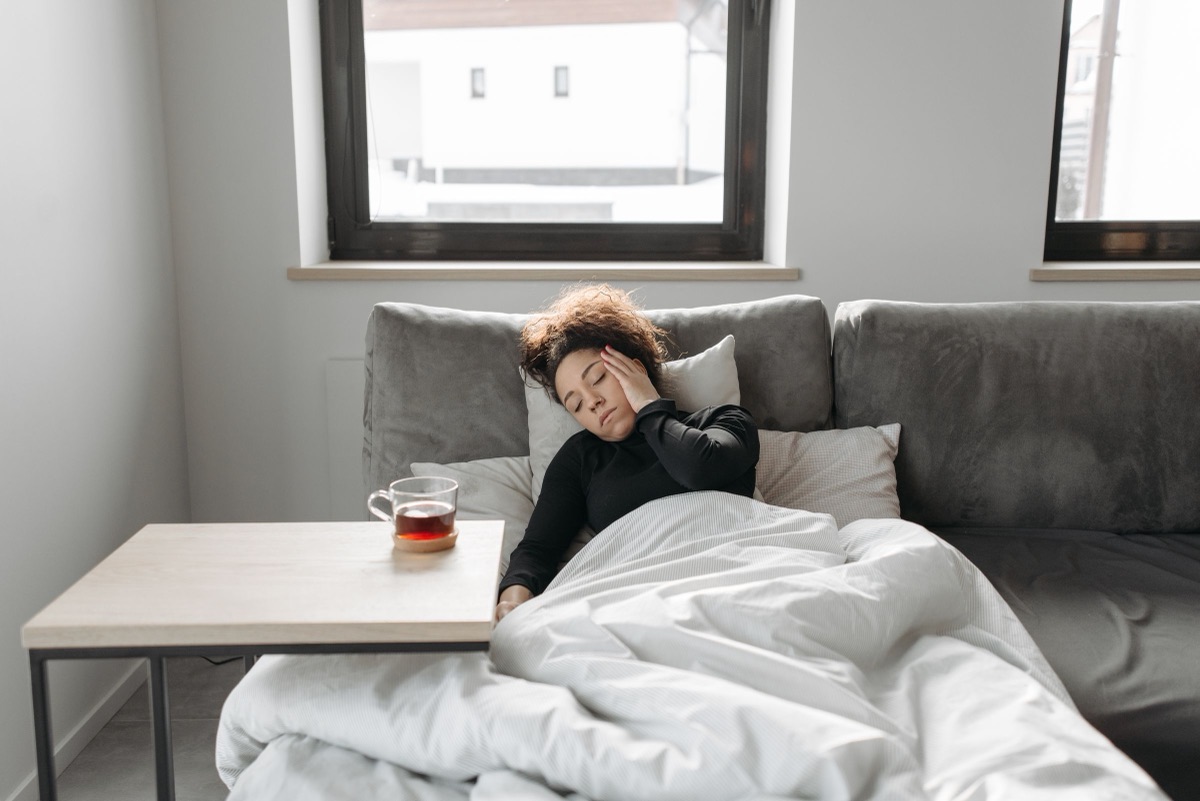 A young woman resting on a sofa under a duvet, feeling unwell