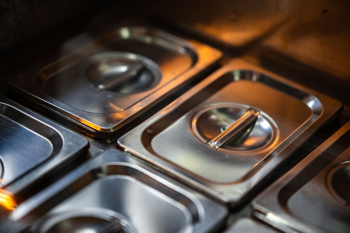 Rows of stainless steel food containers with lids in a professional kitchen